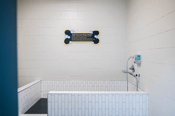 A sign for a self service dog wash hangs on a wall above a white tiled sink.